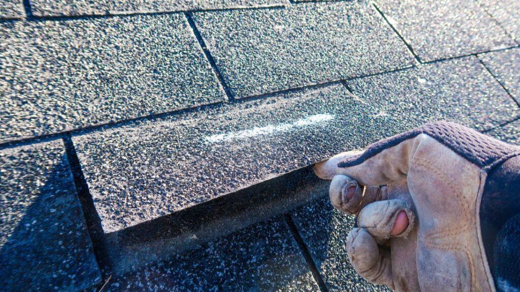 A hand lifting up a shingle on a roof